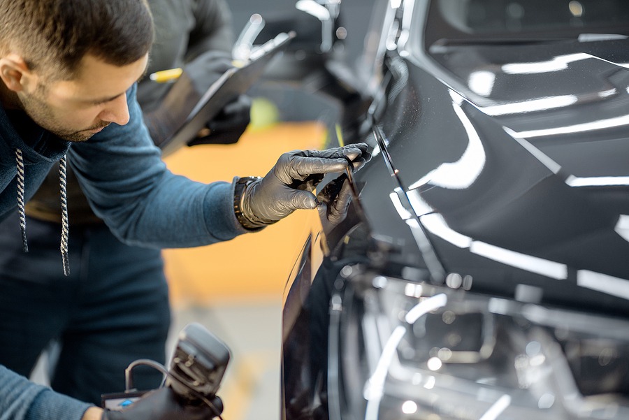 Car service worker examining vehicle body for scratches and damages, taking a car for professional auto detailing. Professional body car inspection concept